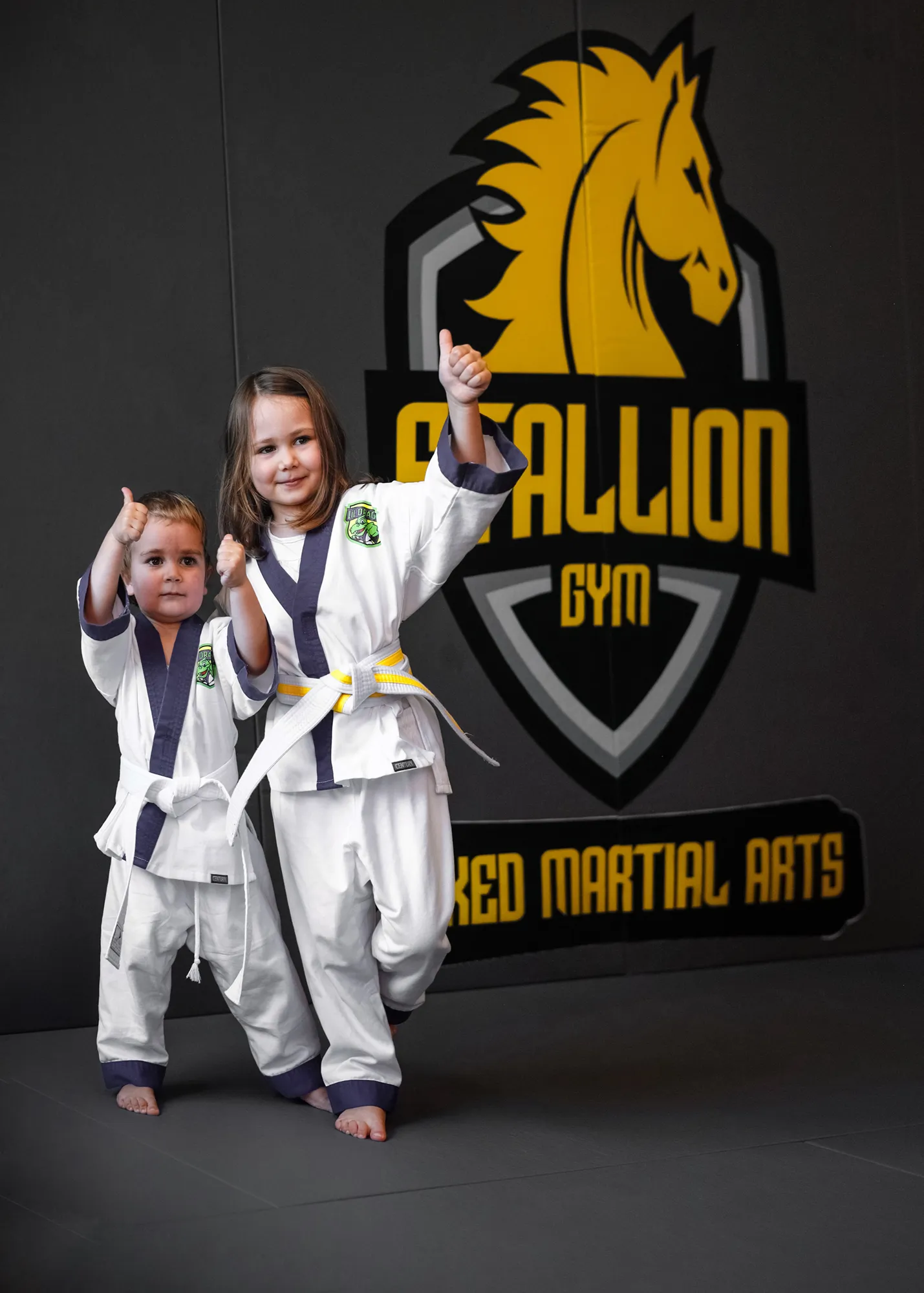 Zwei kleine Kinder im Gi vor dem Stallion Gym Logo